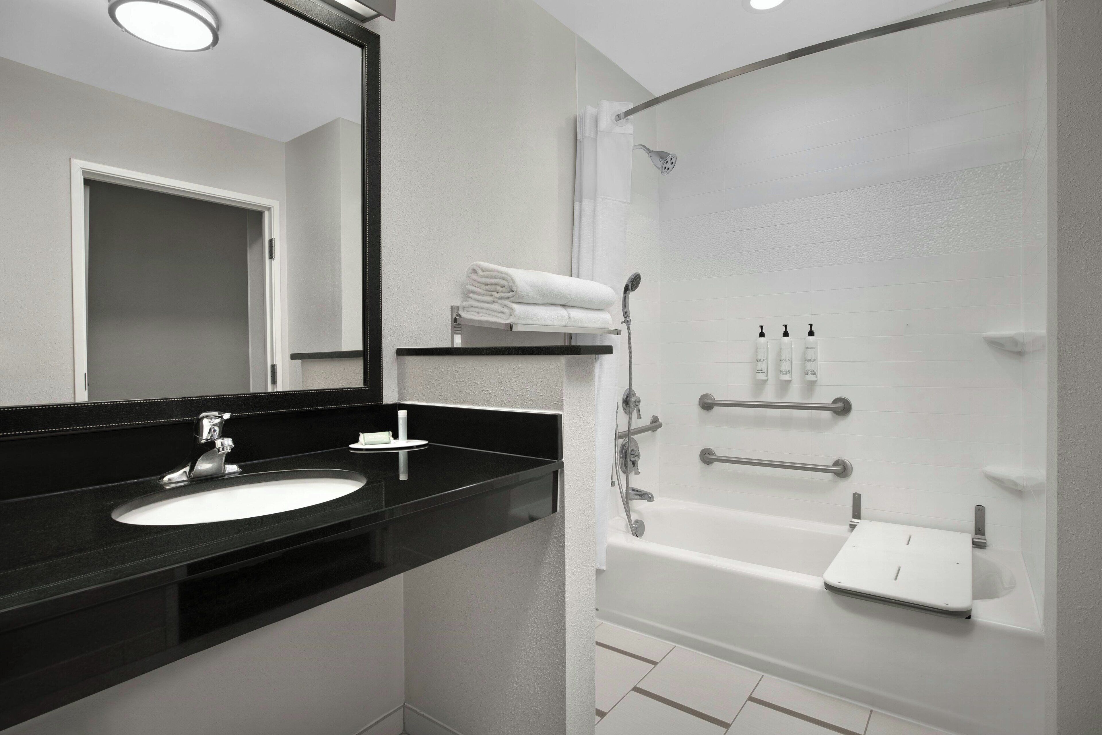 Un baño moderno con lavamanos de encimera negro, bañera blanca y ducha con mampara de vidrio.