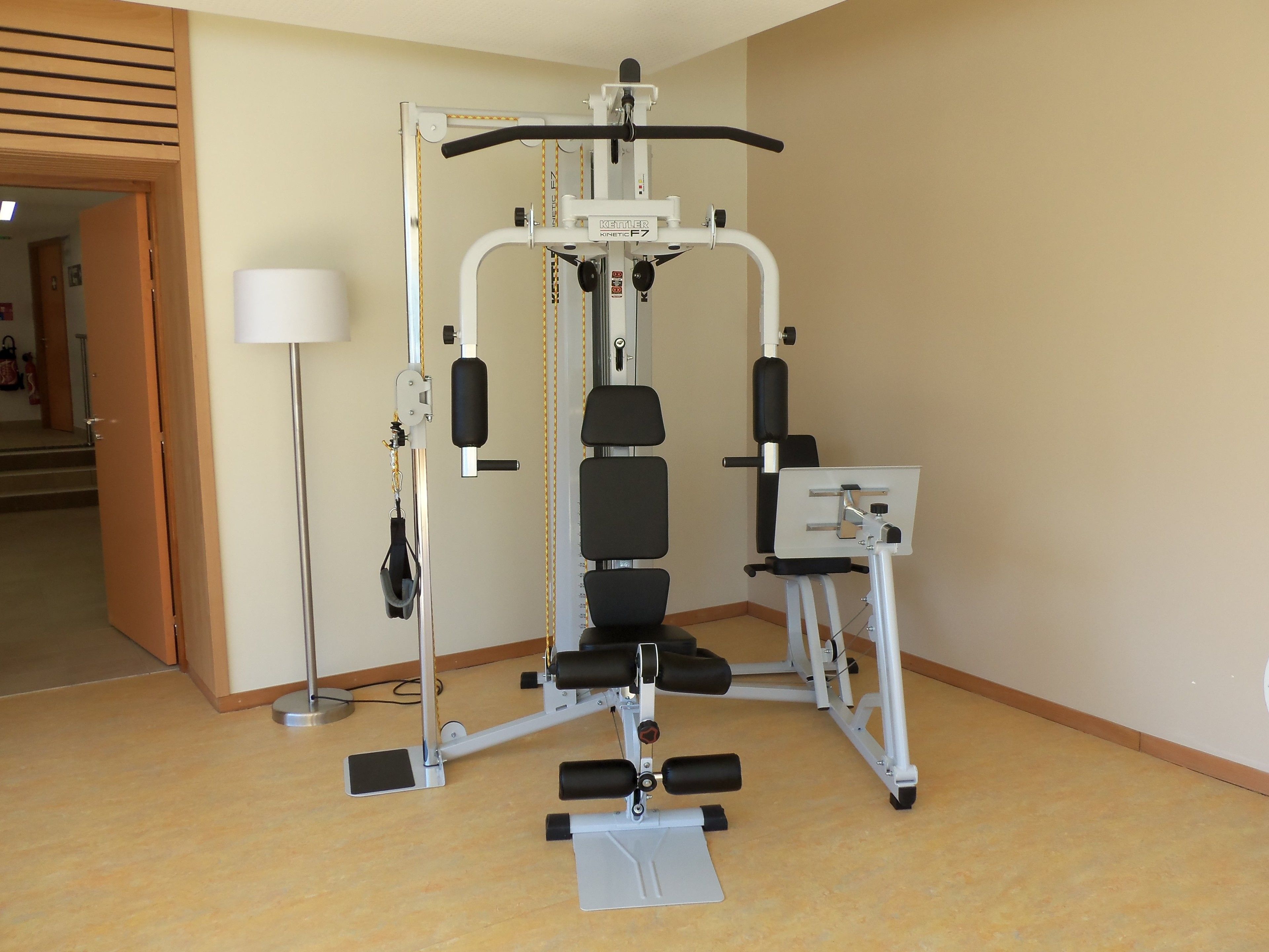 Un gimnasio con una máquina de ejercicio multifuncional, un escritorio de pie y una lámpara.