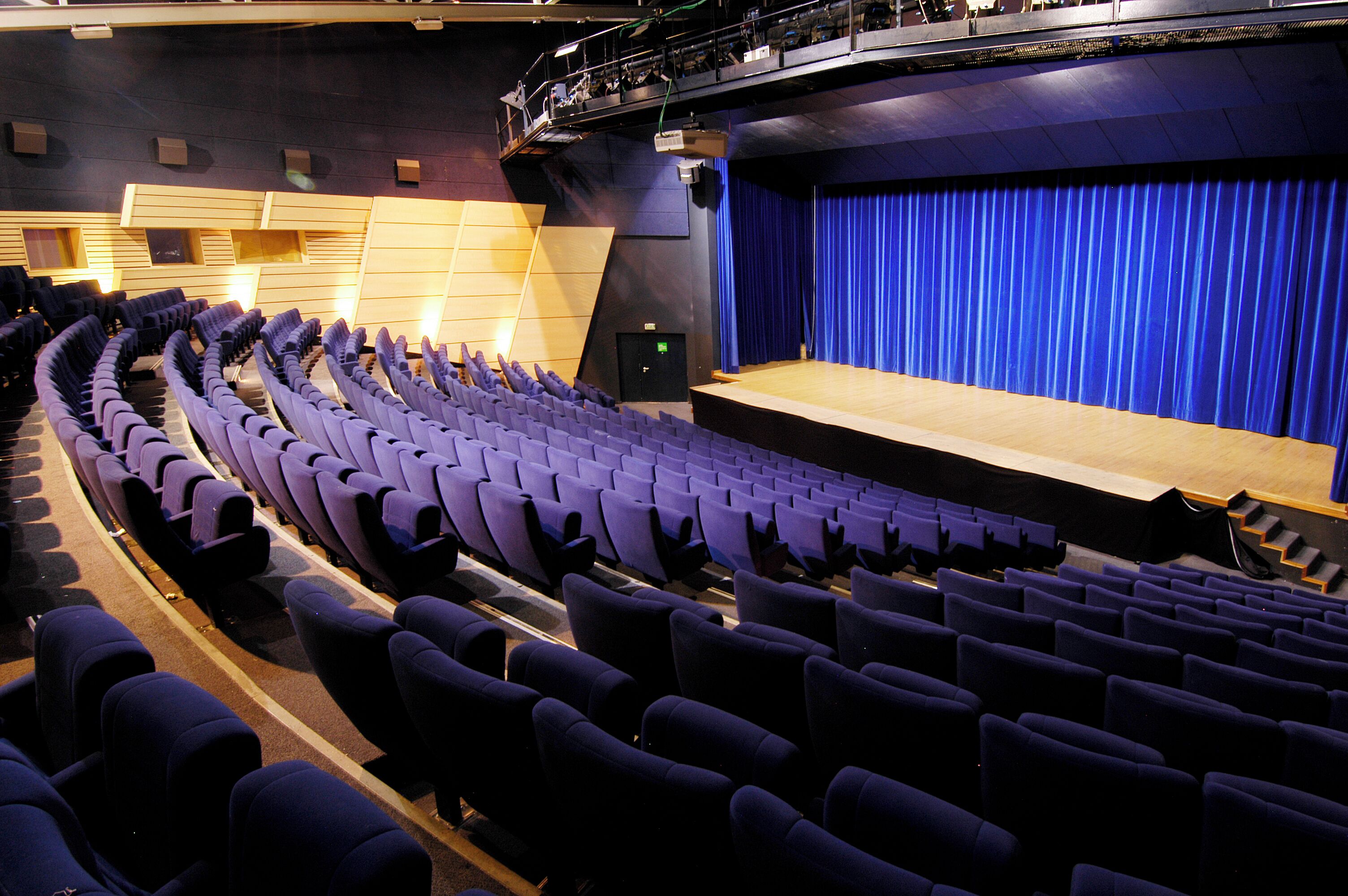 Un auditorio con hileras de asientos, un escenario y un telón de fondo azul.