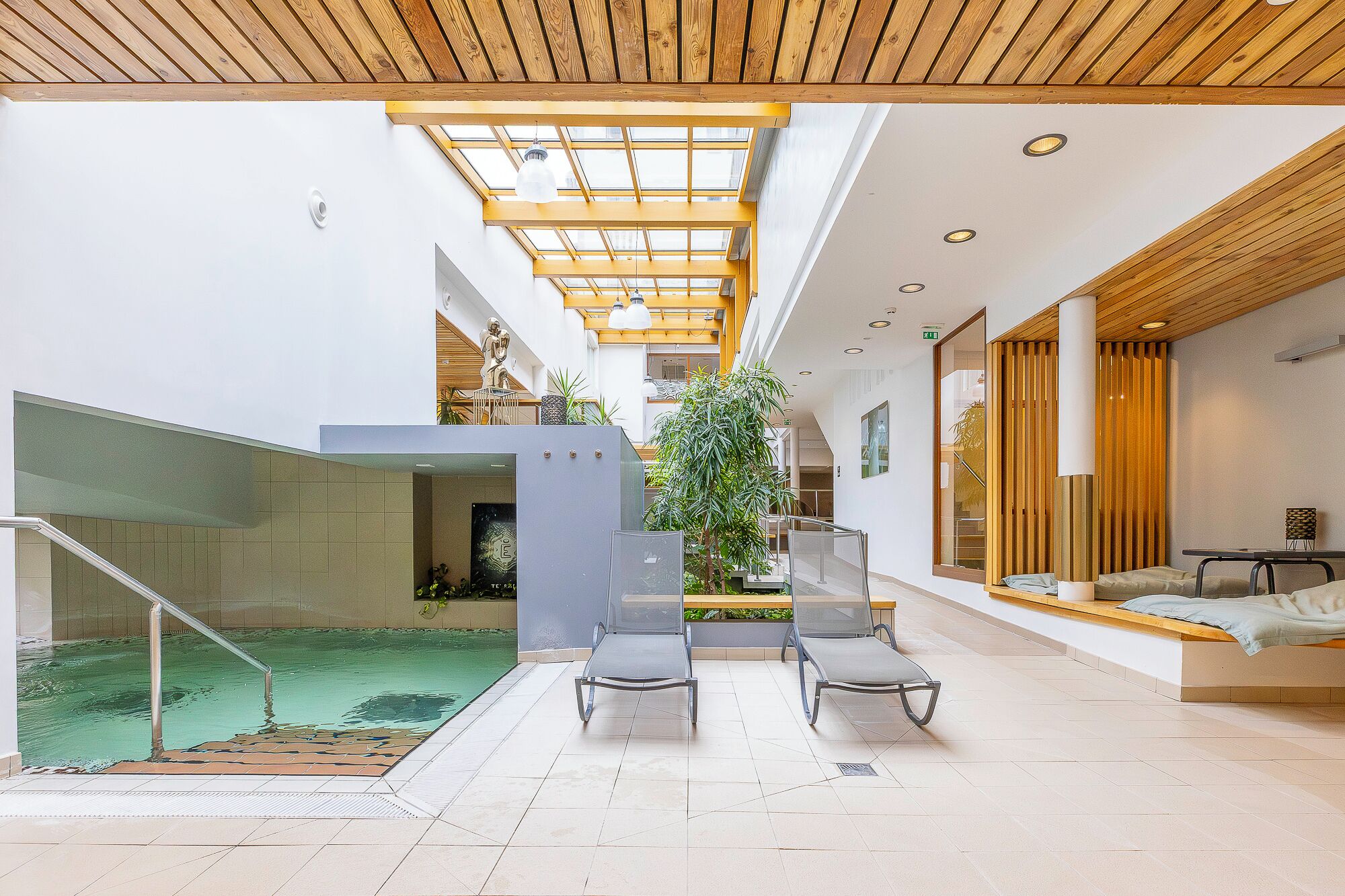 Ein moderner Poolbereich im Innenbereich mit Glaswand, Sitzgelegenheiten und Holzboden.