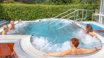 A hot tub with metal railings and a tiled edge, surrounded by greenery.