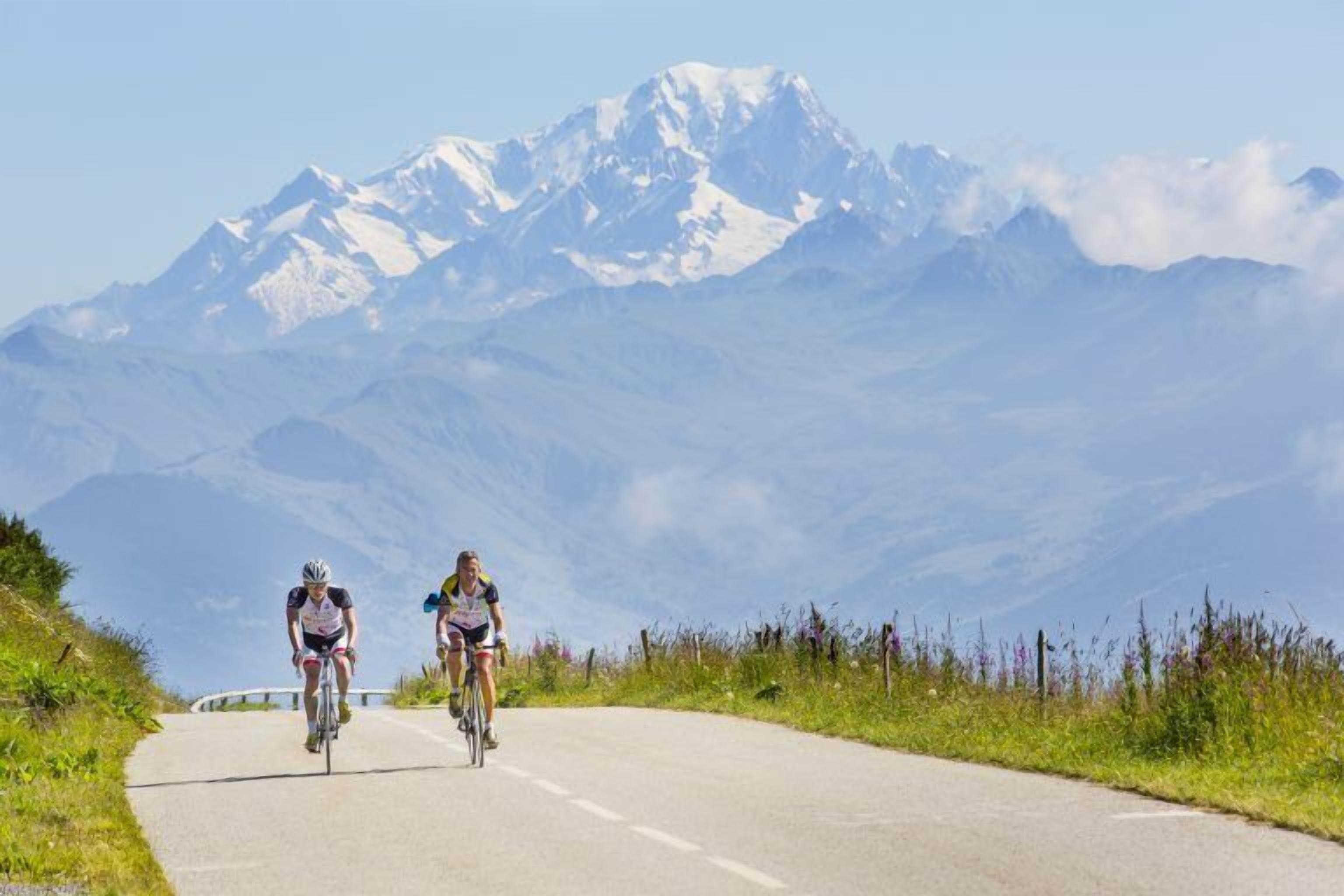 Zwei Radfahrer auf einer asphaltierten Straße vor einer Bergkulisse.