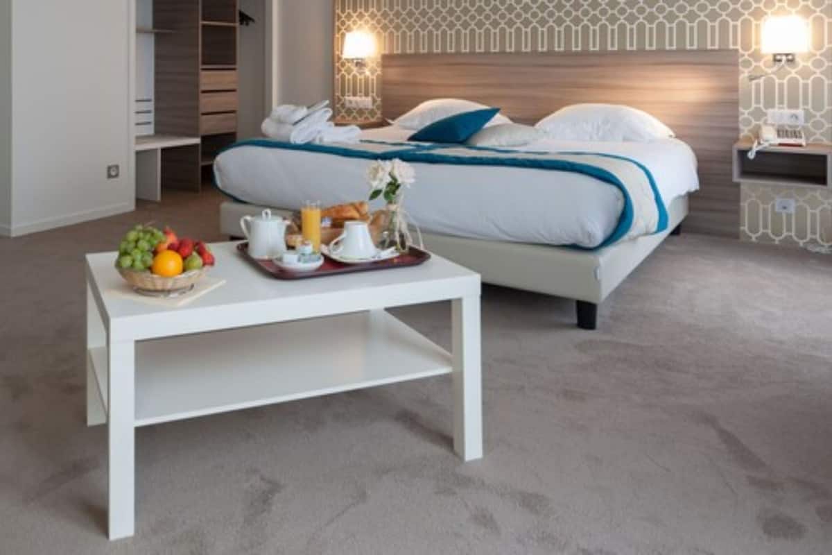 A hotel room with a neatly made bed, a breakfast tray with fruits and pastries, and a bedside table.