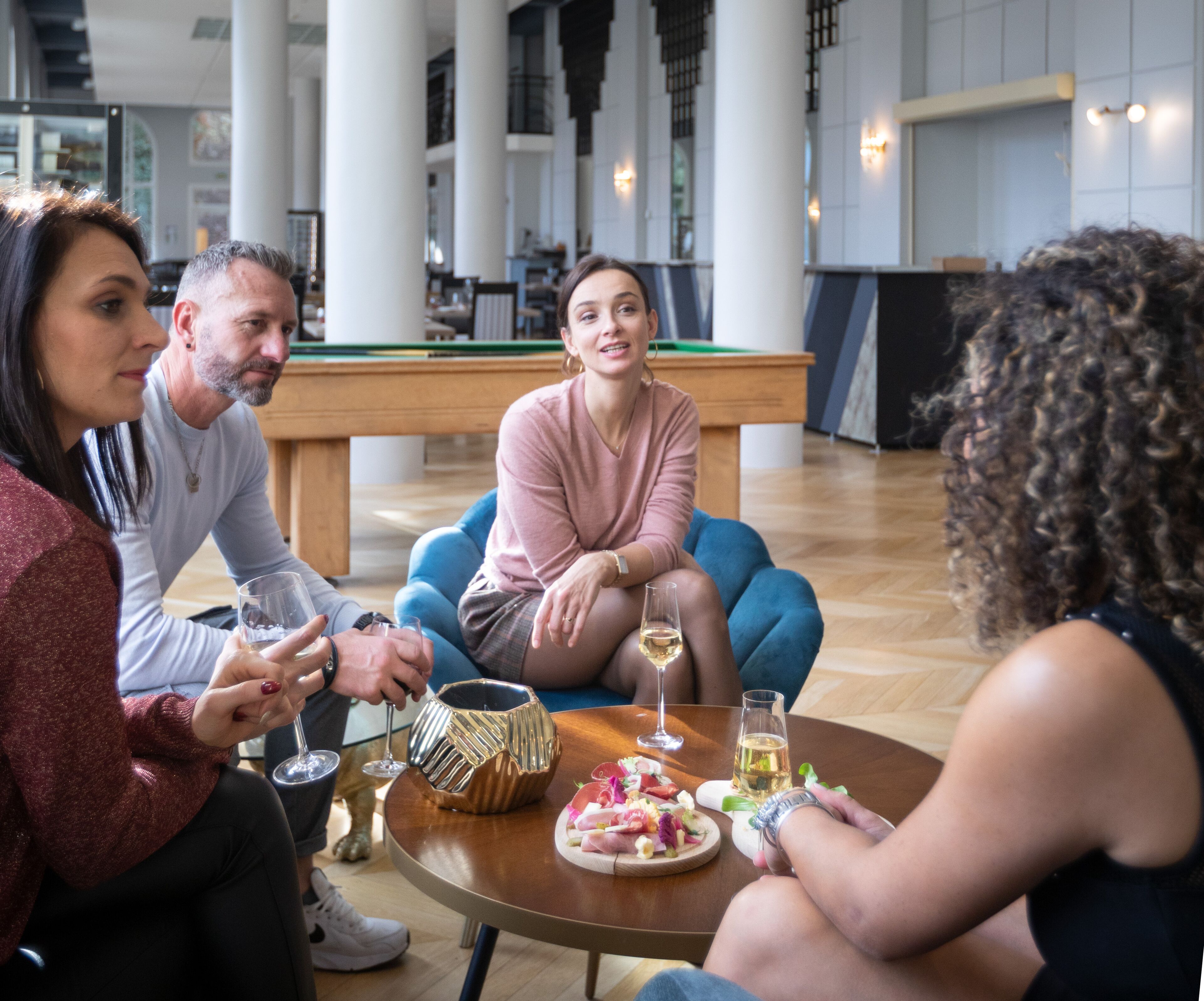 Un grupo de personas sentadas alrededor de una mesa redonda en un espacio interior amplio con techos altos y ventanas grandes.