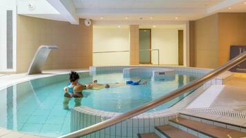 An indoor swimming pool with a person in the water, a pool ladder, and a tiled floor.
