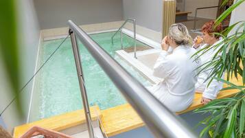 Un área de spa con piscina, asientos de madera y plantas en macetas.