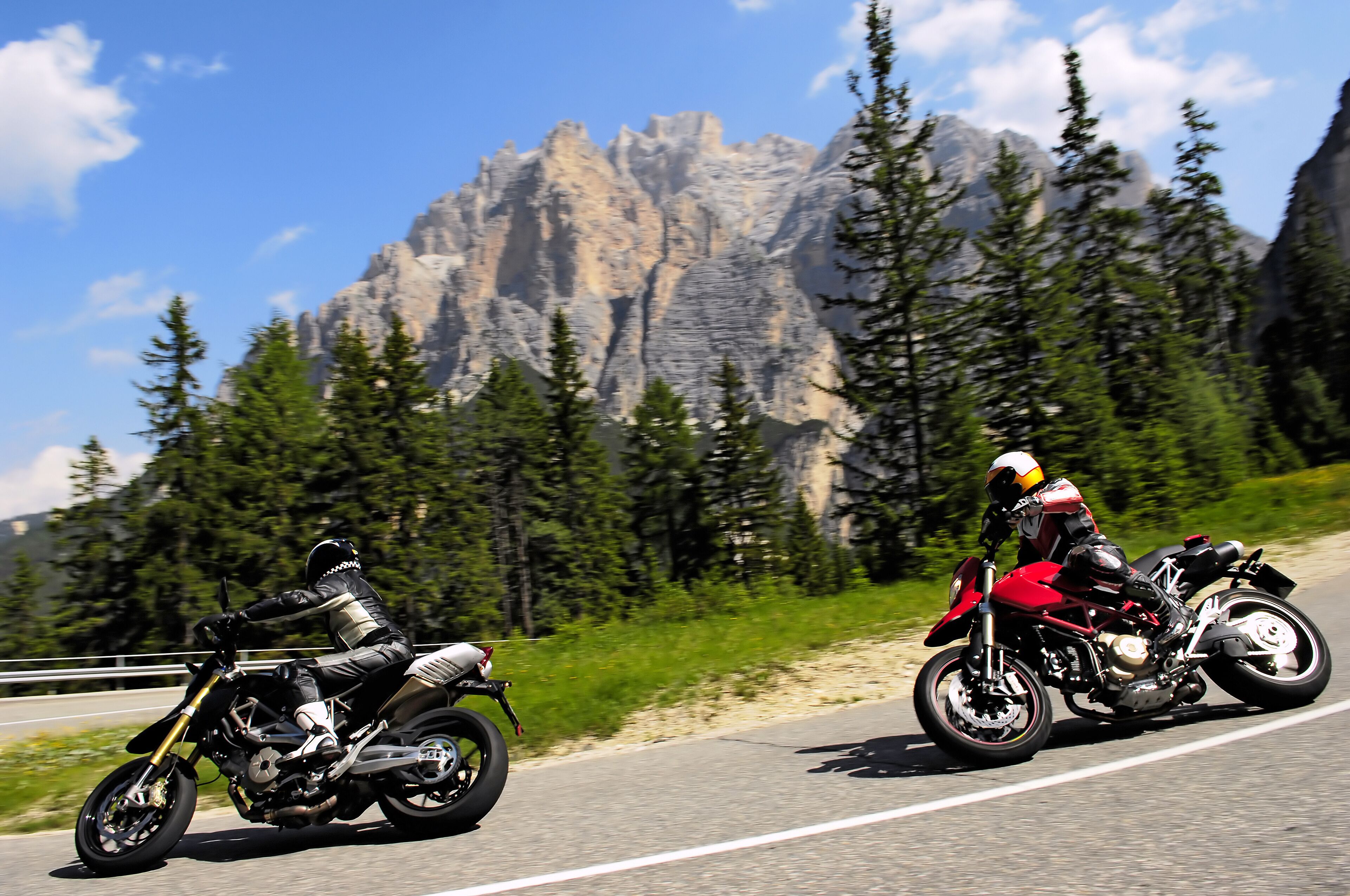 Two motorcyclists on a road with a mountainous backdrop.