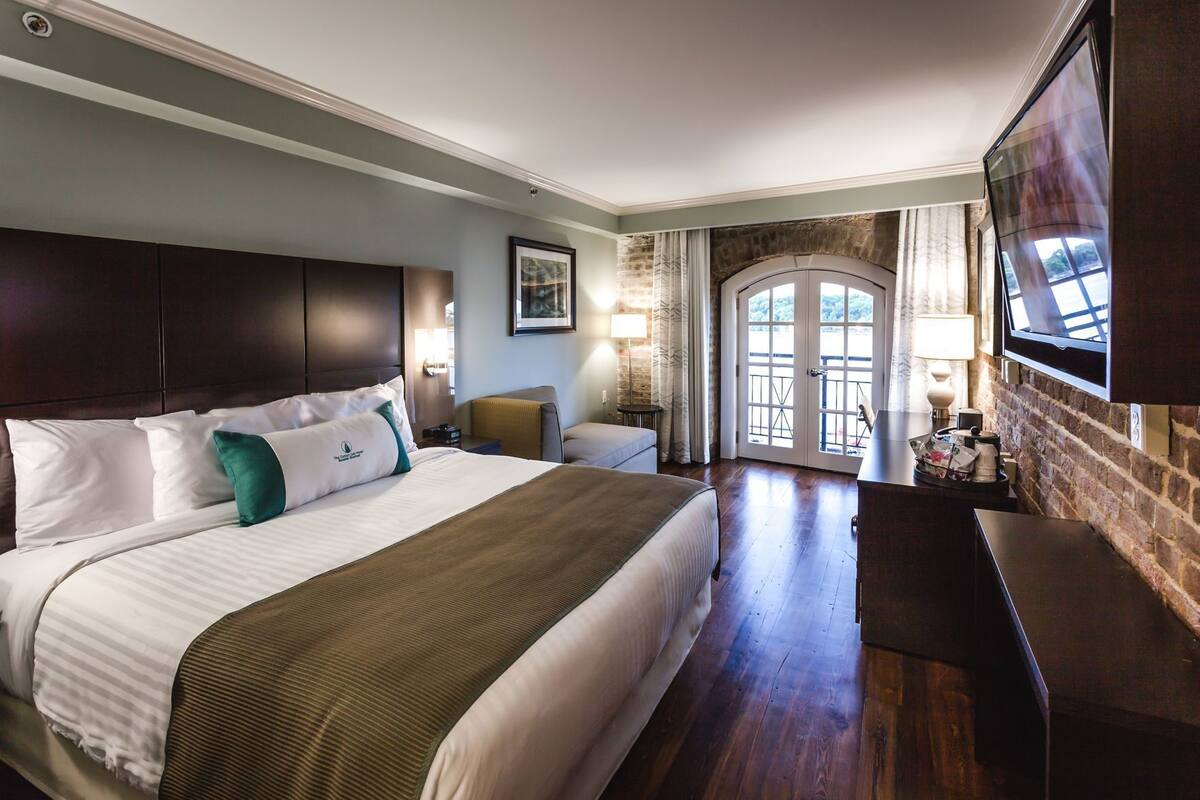A hotel room with a large bed, a TV, a desk, and a balcony with a view.