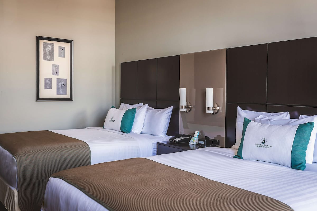 A hotel room with two beds, a framed picture on the wall, and a nightstand with a phone and a lamp.