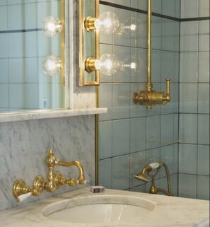 A bathroom with a marble sink, gold fixtures, and a tiled wall. - The Marlton Hotel (New York)