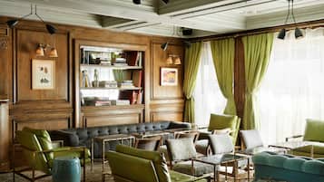 A room with a large sectional sofa, multiple armchairs, a bookshelf, and a window with green curtains.