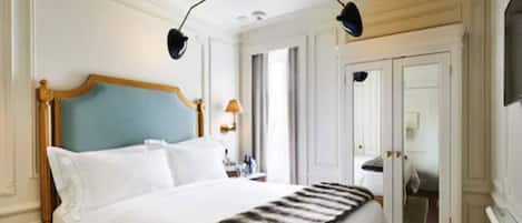 A hotel room with a large bed, a wooden headboard, and a mirror on the wall.