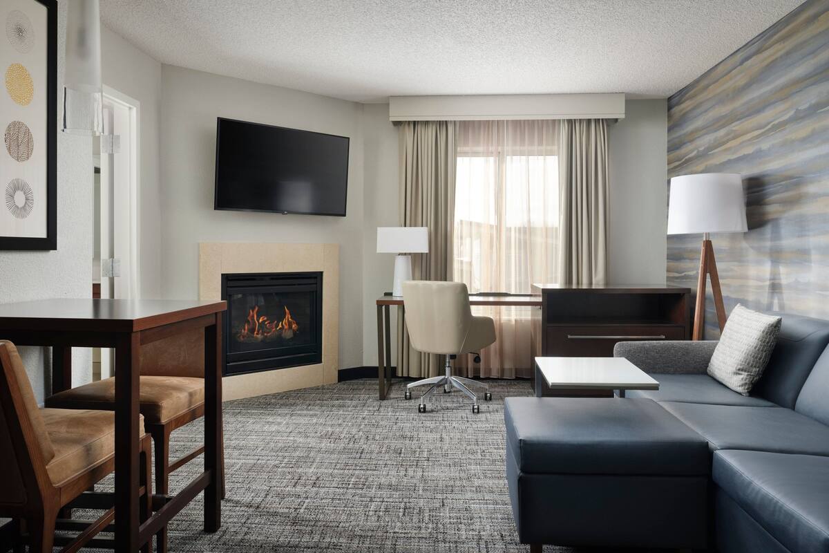 A hotel room with a fireplace, a flat-screen TV, a sofa, a desk, and a chair.