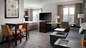Una habitación de hotel con cama, escritorio con televisor, sofá y zona de comedor con sillas.