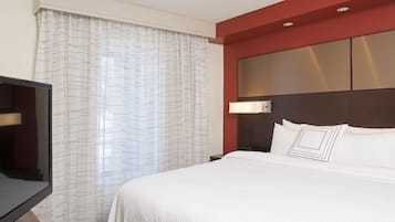 A hotel room with a large bed, a TV, and a window with curtains.
