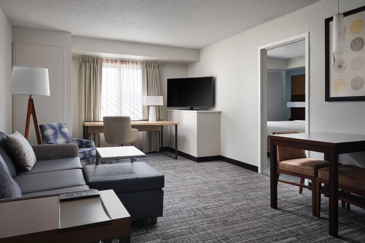 A hotel room with a sofa, a desk with a TV, a chair, and a bed.