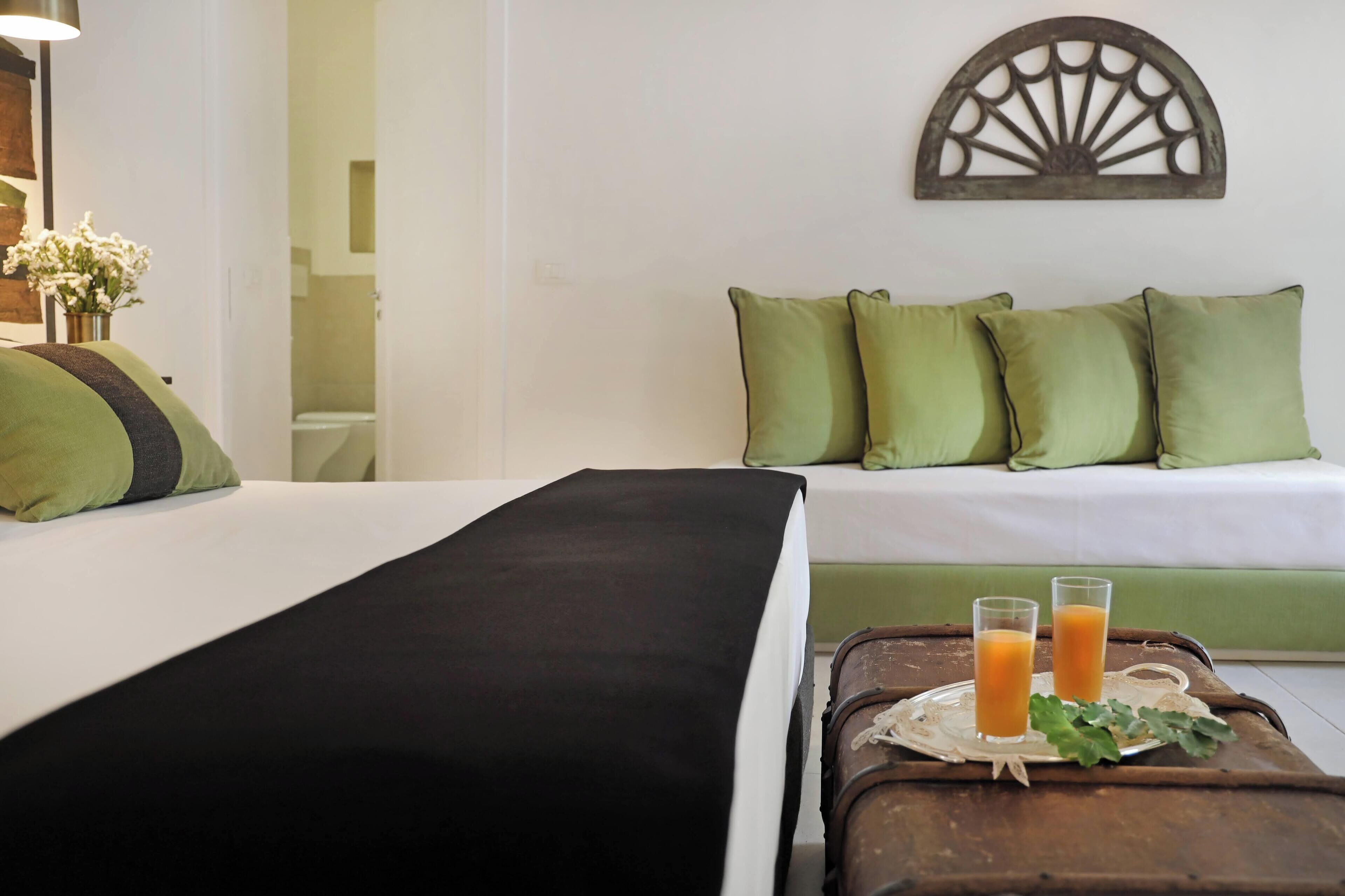 A hotel room with a bed, a green sofa, and a tray with two glasses of orange juice.