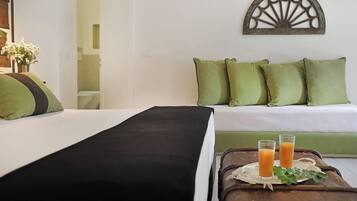 A hotel room with a bed, a green sofa, and a tray with two glasses of orange juice.