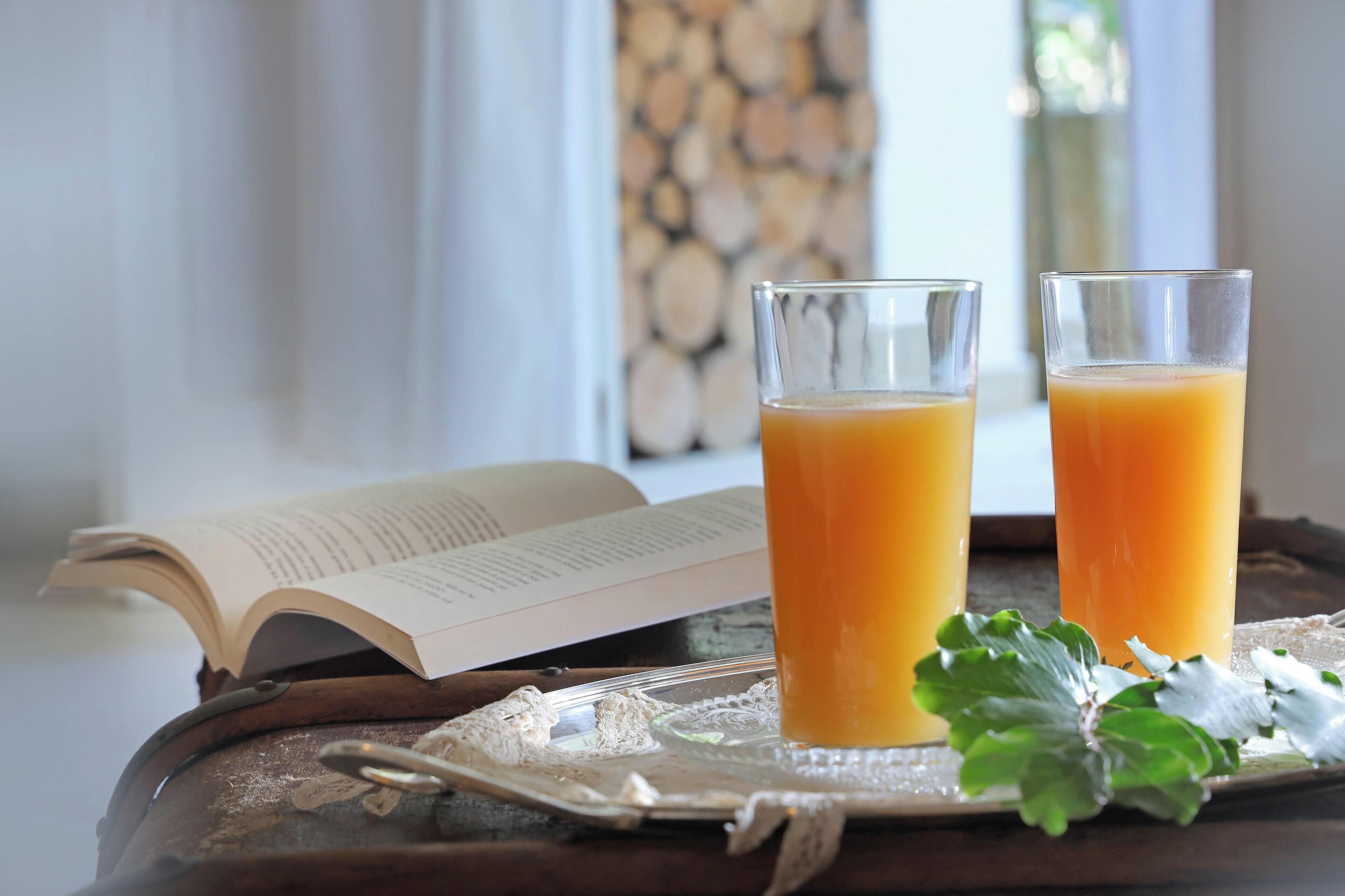 Two glasses of orange juice on a tray with a book and a decorative leaf.