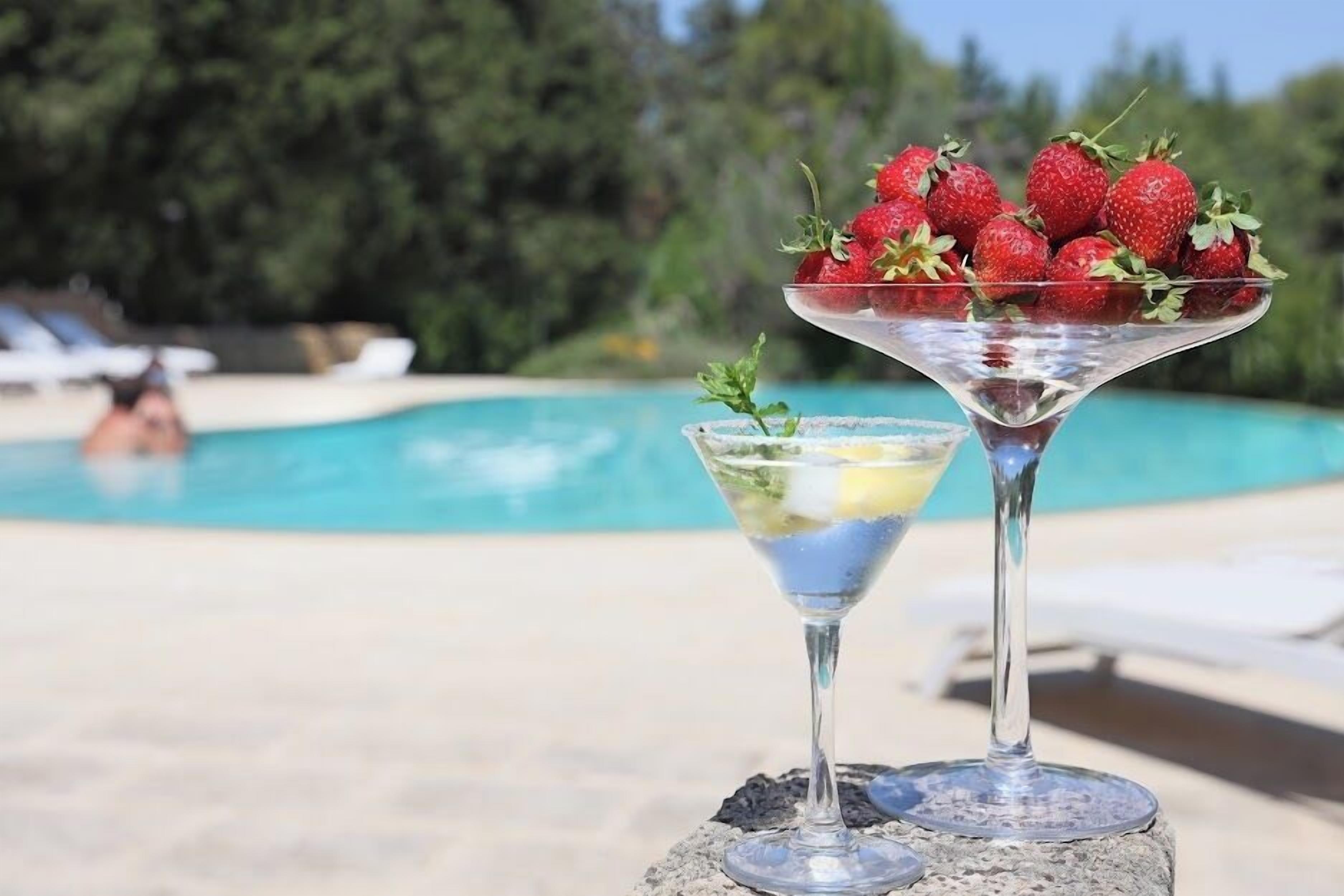 Zona de piscina con vista despejada a la piscina, sillas de descanso y una zona de bar con una copa de martini y un bol de fresas.