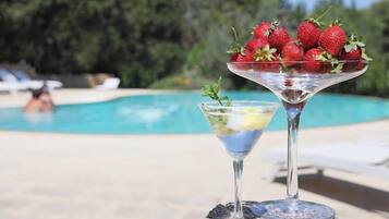 Zona de piscina con vista despejada a la piscina, sillas de descanso y una zona de bar con una copa de martini y un bol de fresas.