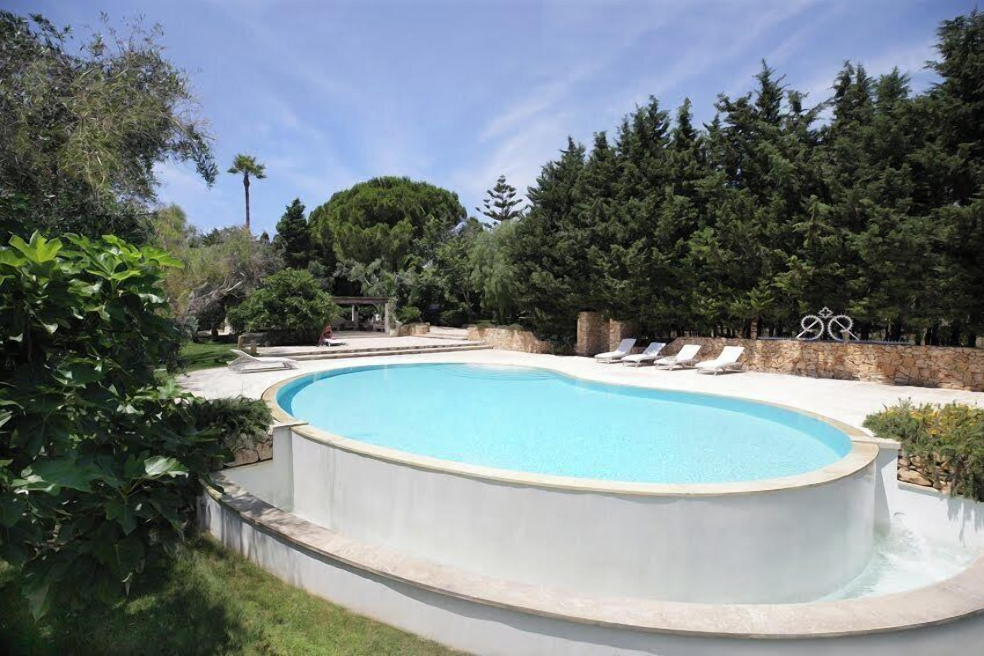 A swimming pool with a curved edge, surrounded by a stone wall and lush greenery.