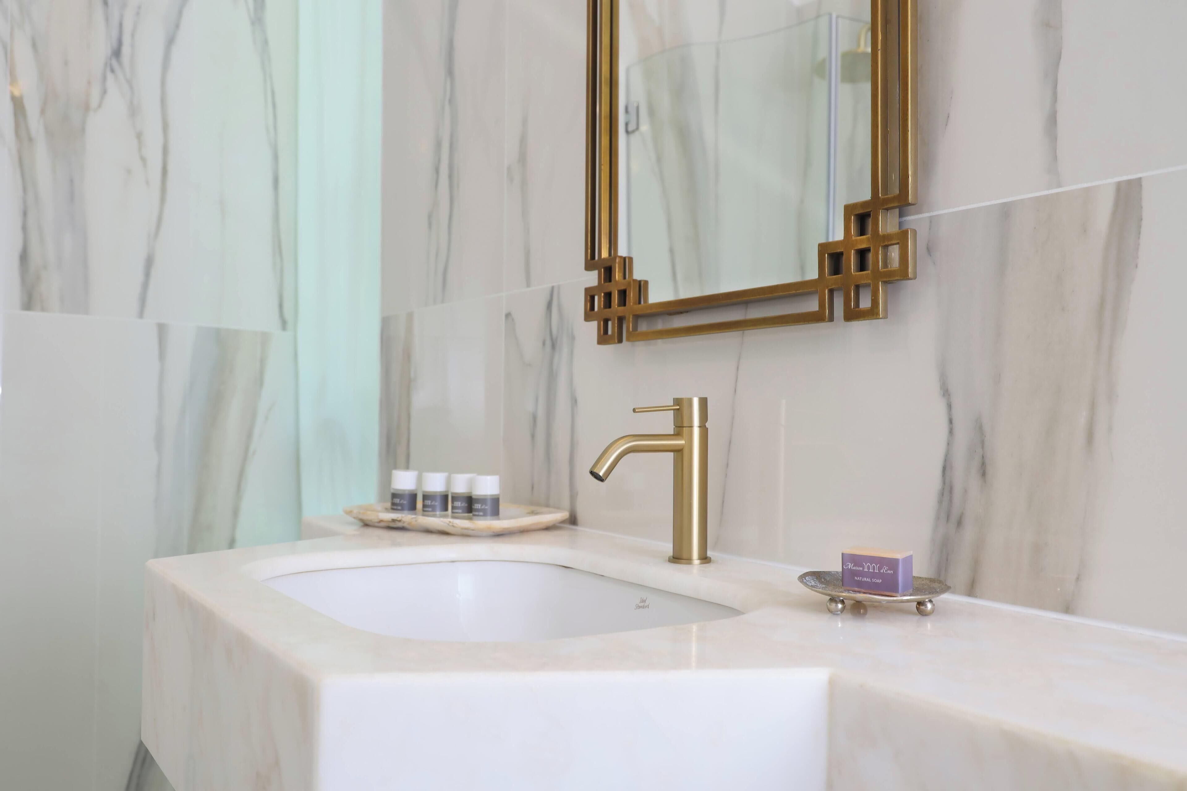 Ein Badezimmer mit Marmorwaschbecken, Goldarmatur und einer kleinen Seifenschale mit einem violetten Stück Seife.