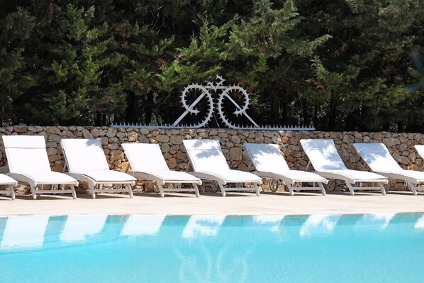 A poolside area with white lounge chairs and a stone wall. - Maison d'Enrì (Gallipoli)