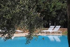 A pool with white lounge chairs, surrounded by trees and a stone wall. - Maison d'Enrì (Gallipoli)