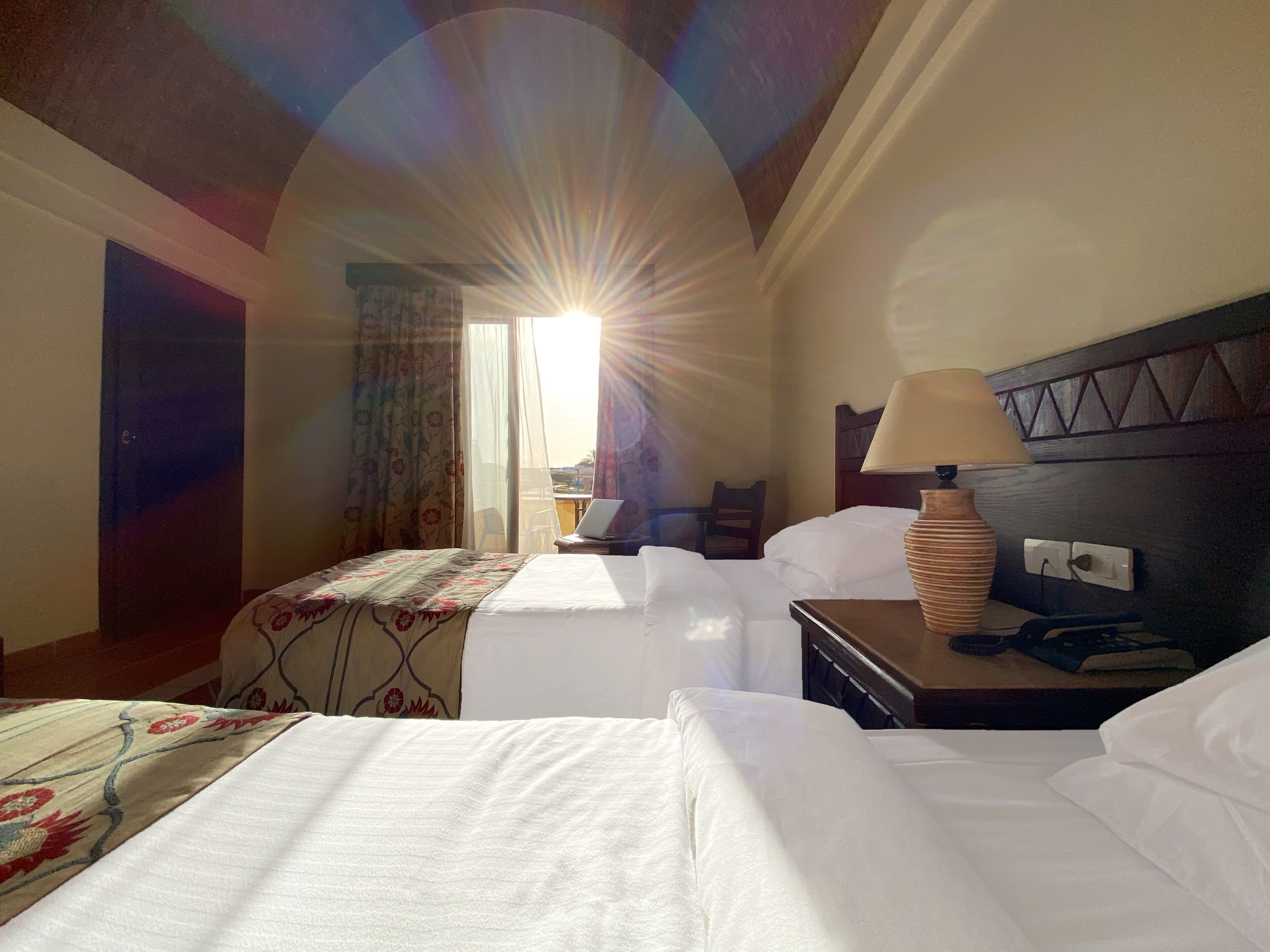 Habitación de hotel con dos camas, un escritorio con lámpara, una silla y una ventana con cortinas.