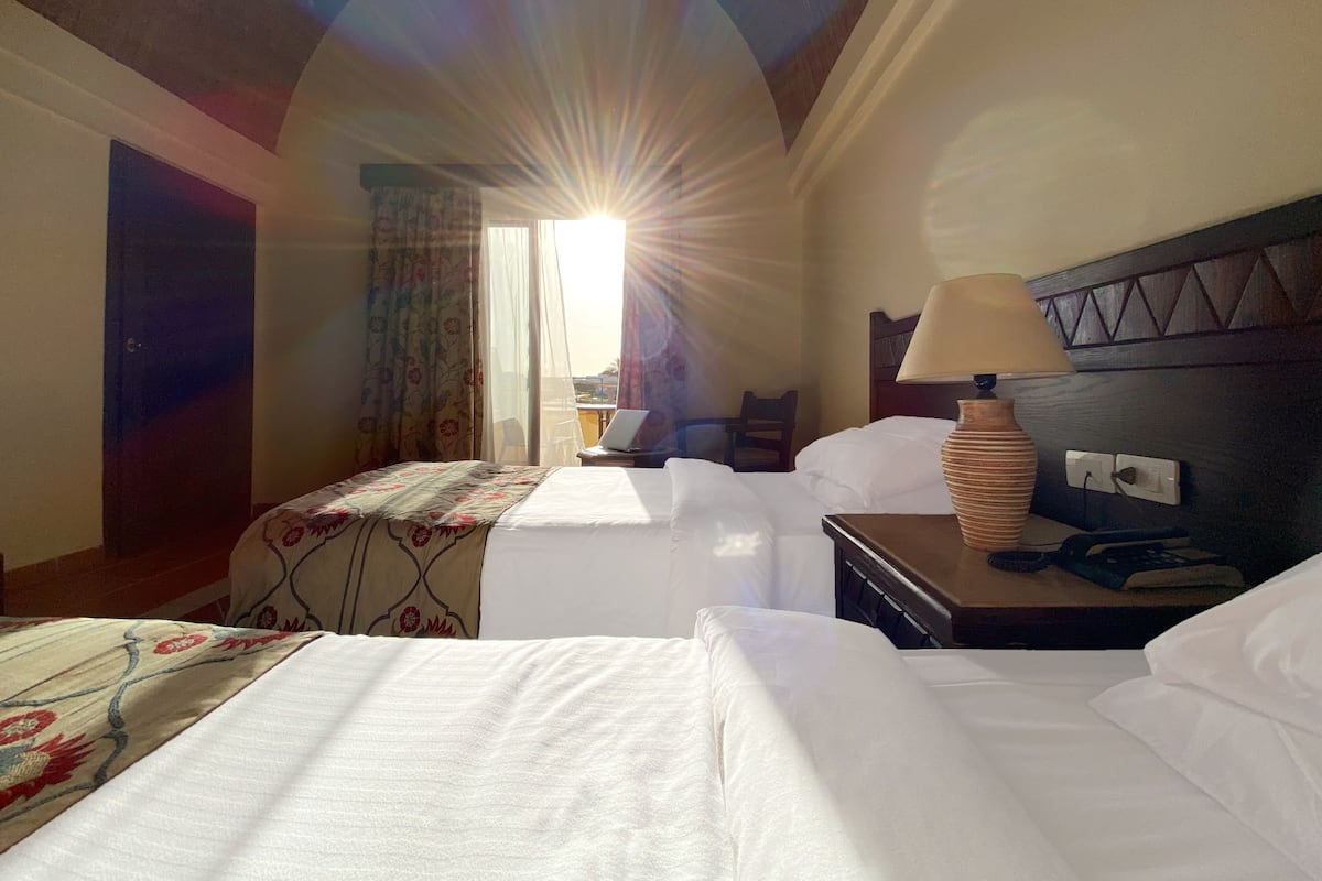 Ein Hotelzimmer mit zwei Betten, einem Schreibtisch mit Lampe, einem Stuhl und einem Fenster mit Vorhängen.