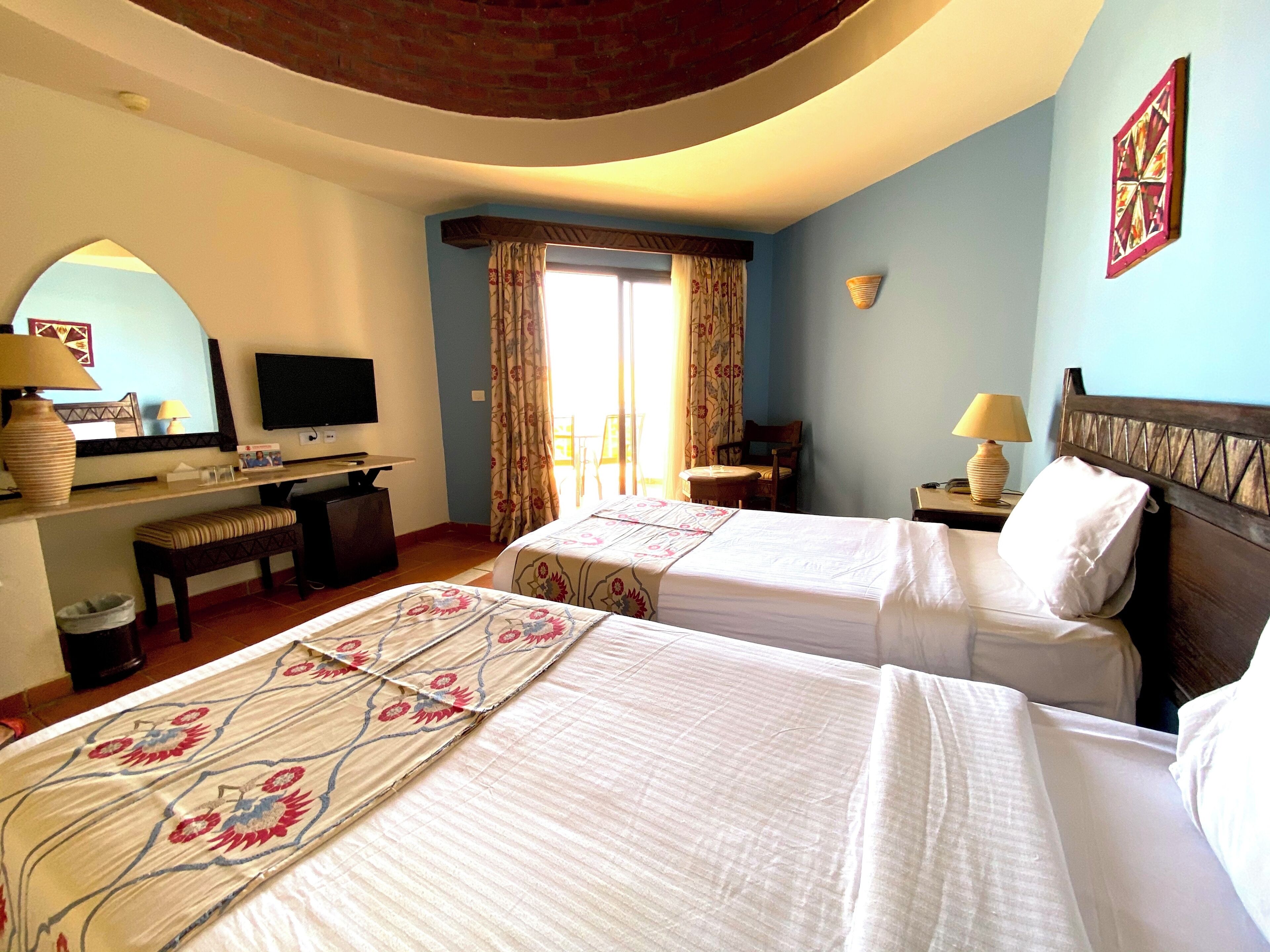 Habitación de hotel con dos camas, un escritorio, un televisor y una ventana con cortinas.