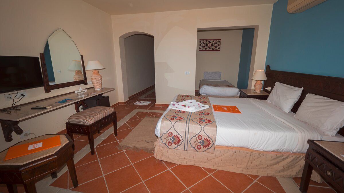 Una habitación de hotel con cama, escritorio, silla, televisor y espejo.