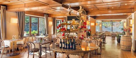 Un comedor amplio con piso de madera, mesas redondas y sillas. Hay una mesa central con botellas y una decoración.