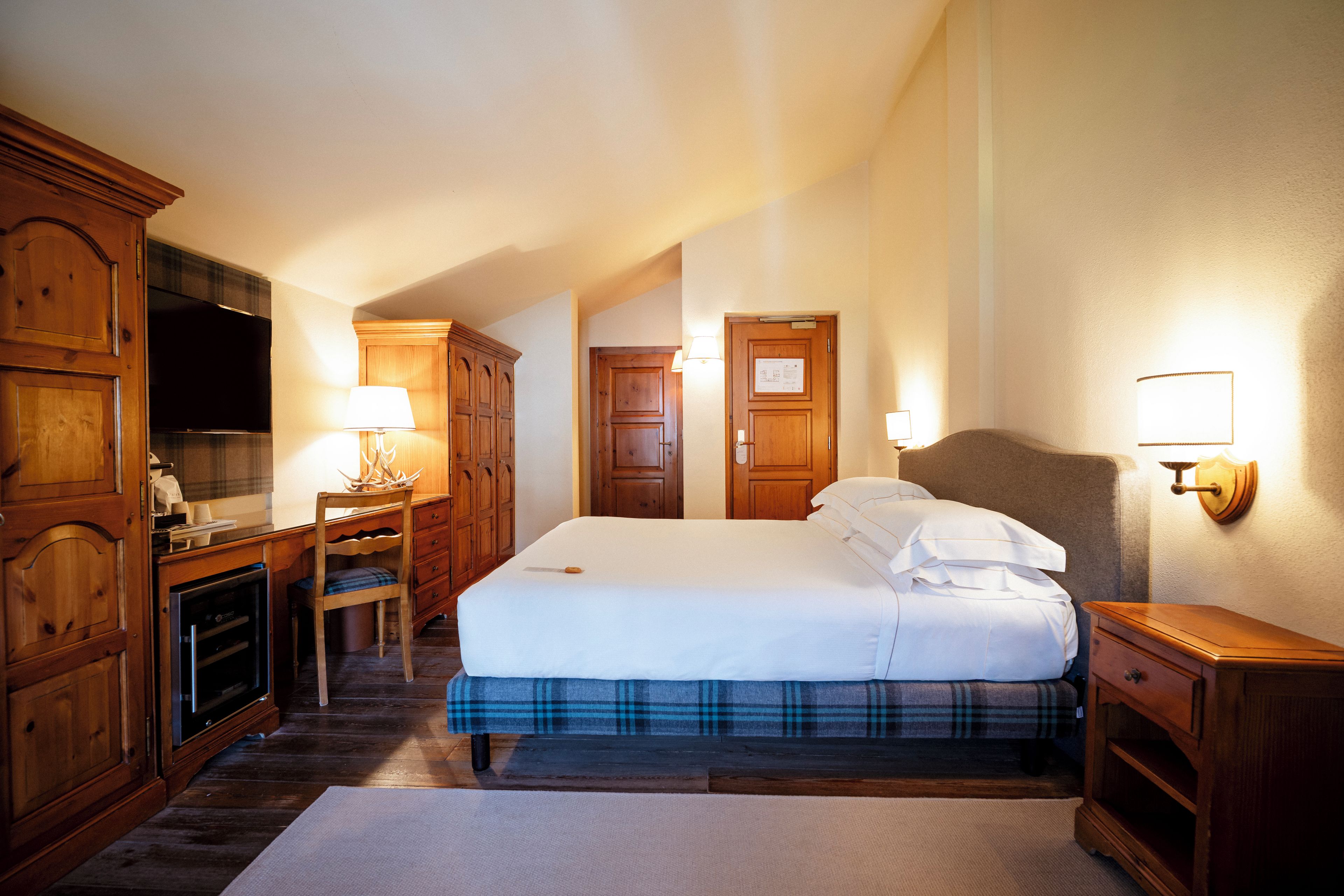 A hotel room with a bed, a desk, a television, and wooden furniture.