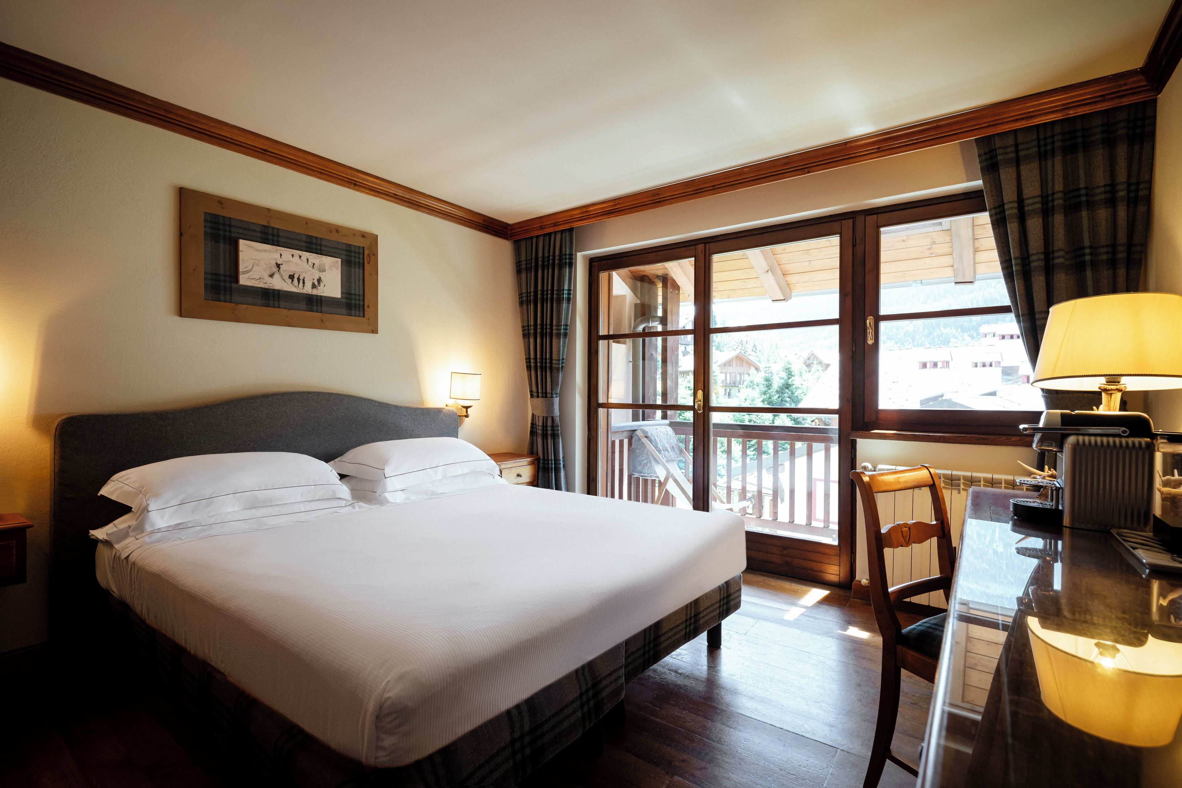 Une chambre d’hôtel avec un grand lit, un bureau avec une lampe et une fenêtre avec des rideaux.