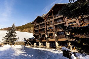 Una cabaña de varios pisos con balcones, una pista de esquí al fondo y terreno cubierto de nieve.
