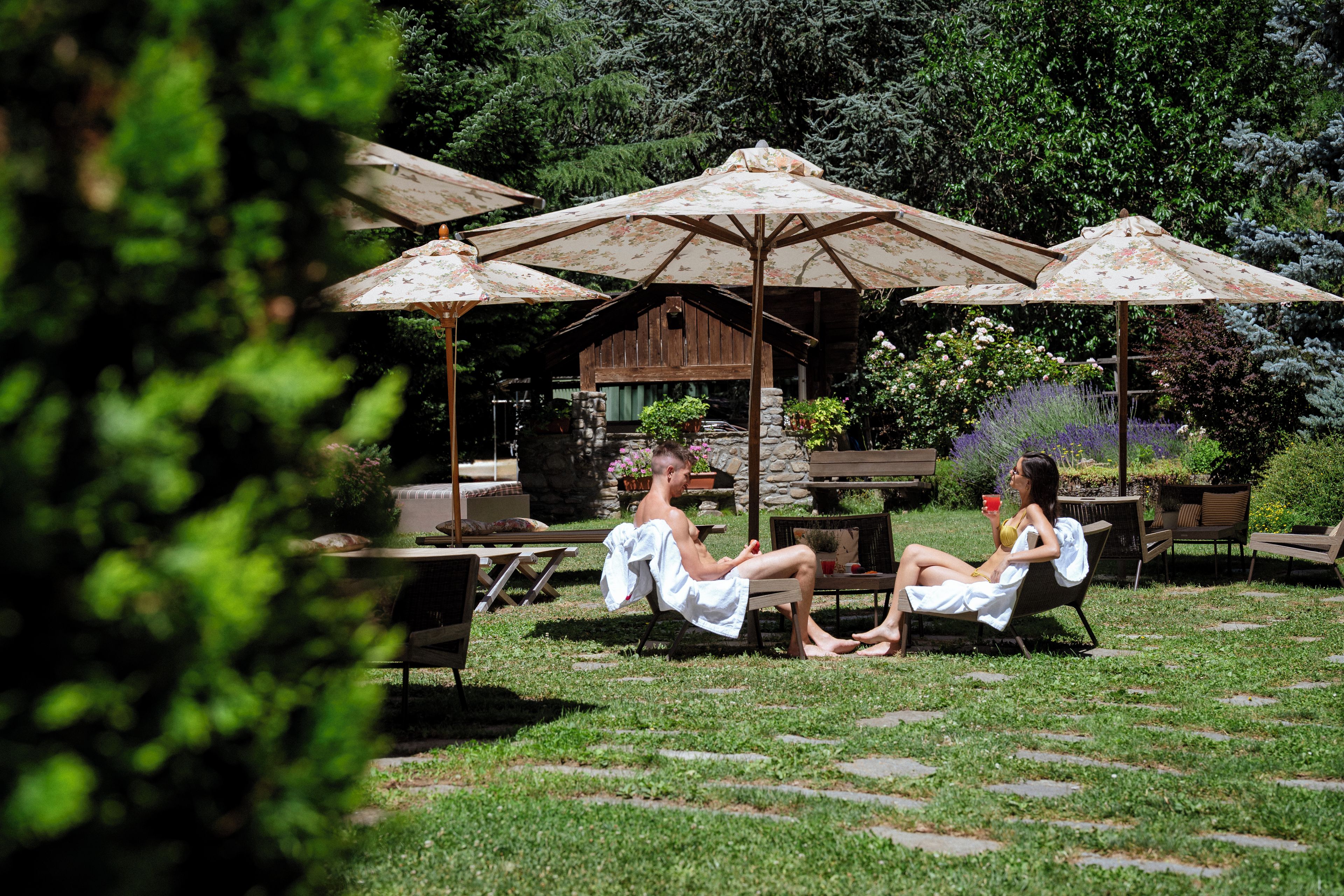 Zona salotto all'aperto con ombrelloni, una struttura in pietra e un giardino.