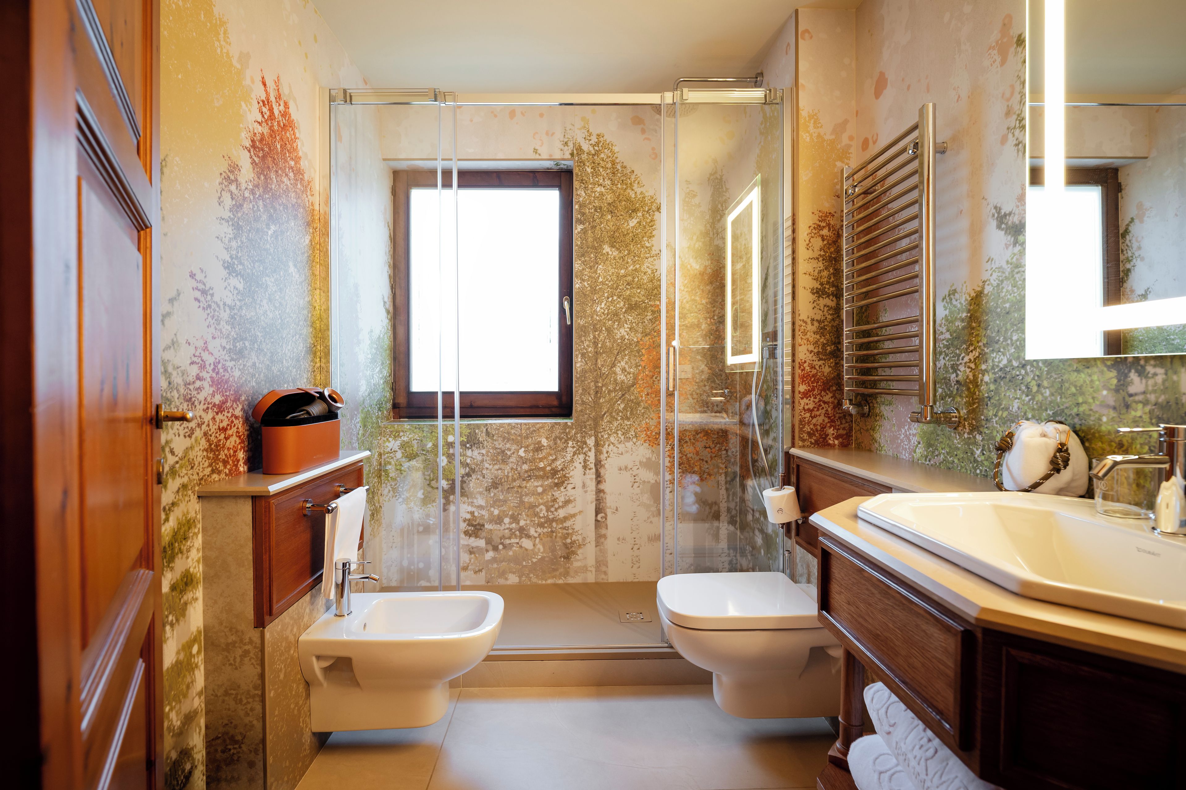 A bathroom with a glass shower enclosure, a bidet, a sink, and a mirror.