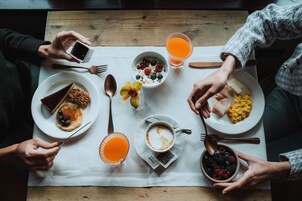 Un desayuno con diferentes platos, como tortitas, huevos revueltos y una rebanada de pastel, sobre una mesa de madera.