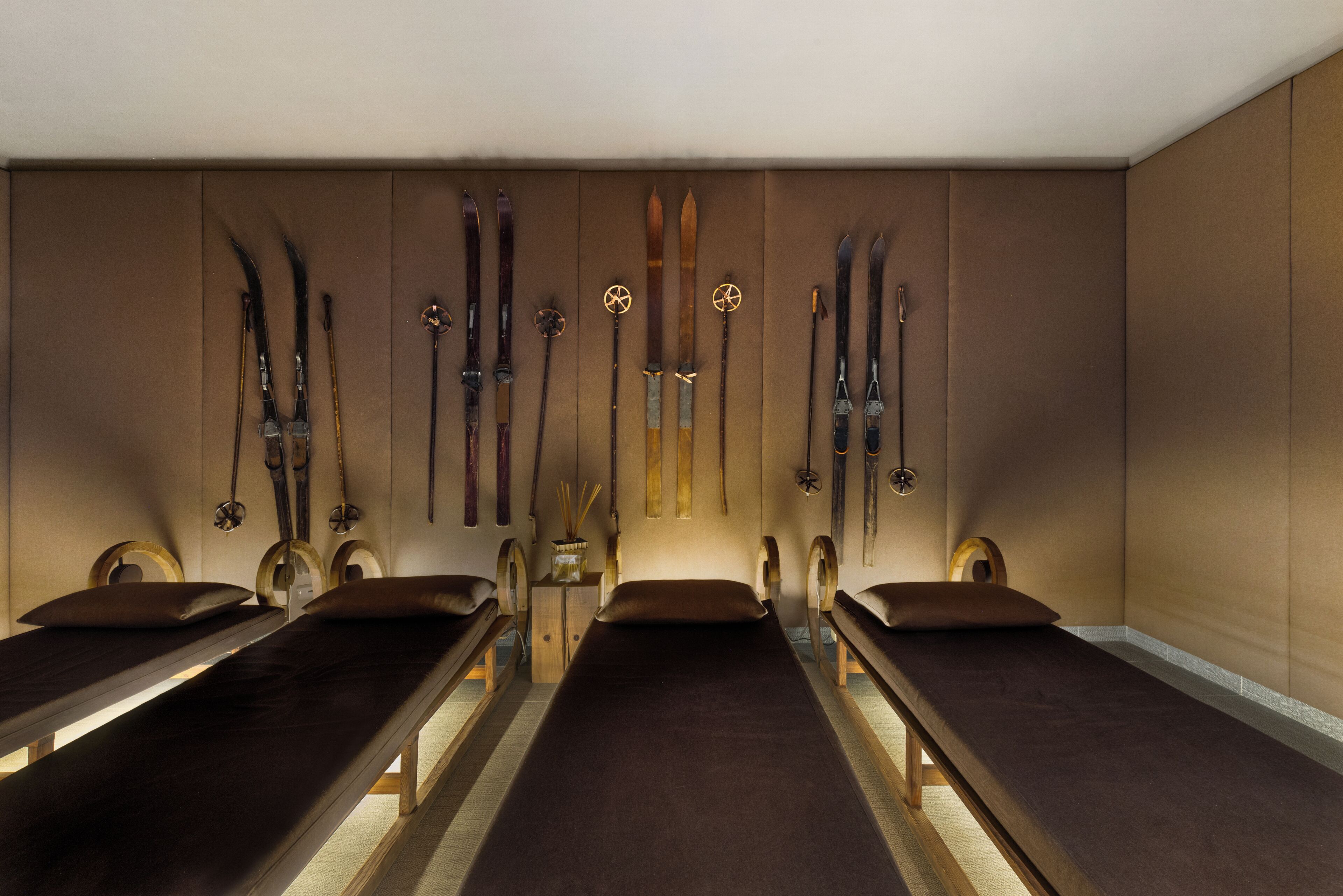 A room with four wooden benches, a wall-mounted ski rack, and a small table with a lamp.