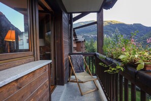 Un balcon en bois avec une chaise, un pot de fleurs et une vue sur les montagnes.