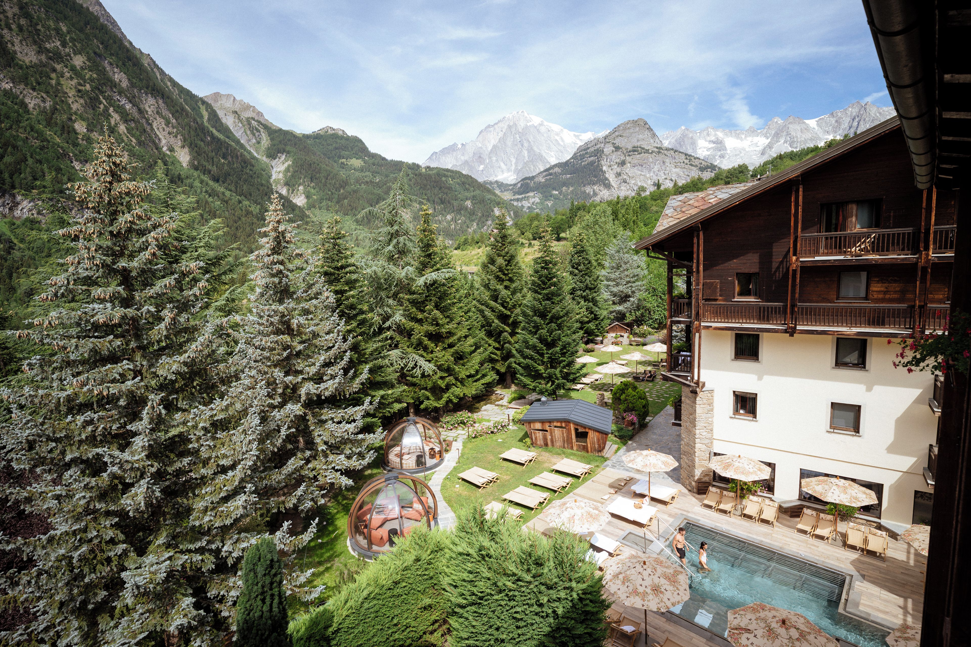 A mountain lodge with a pool, outdoor seating, and a view of the surrounding forest and mountains.