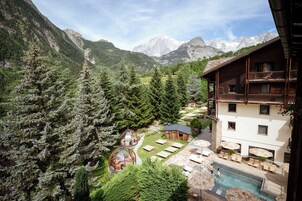 Una cabaña de montaña con piscina, mobiliario exterior y vistas al bosque y las montañas circundantes.