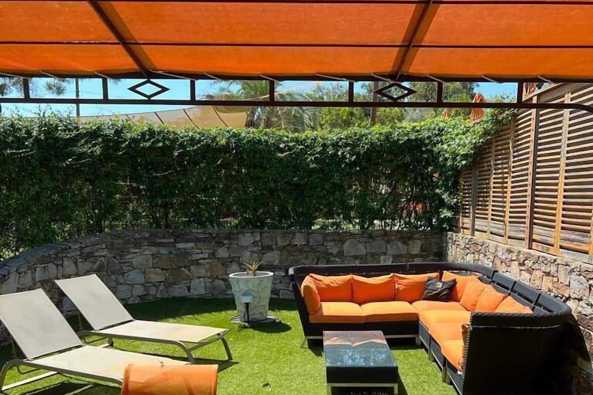 An outdoor patio area with a stone wall, a stone planter, a sofa set, a dining table, and chairs.