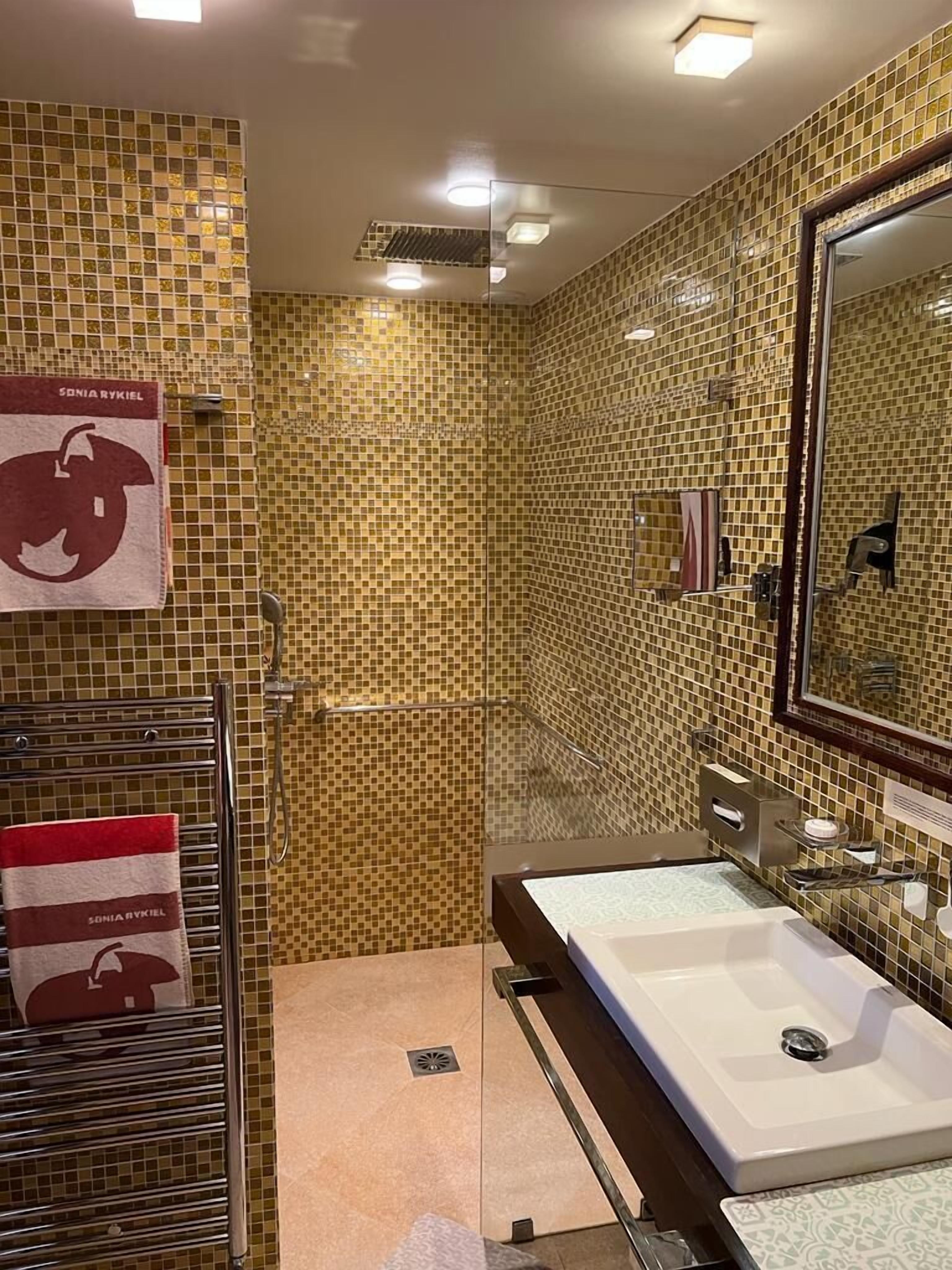 Une salle de bain avec un mur recouvert d’une mosaïque, un grand miroir, un lavabo et un espace douche.