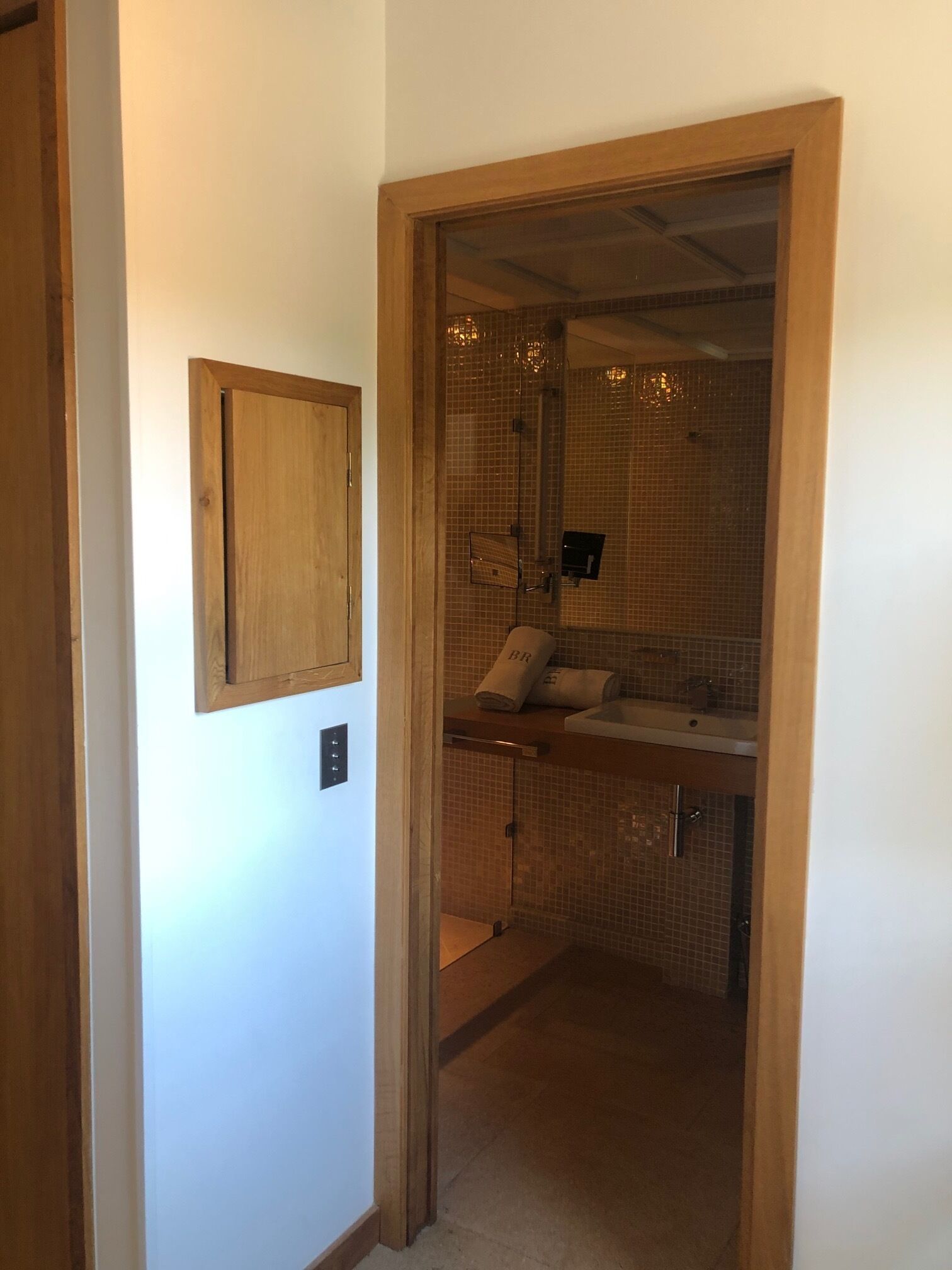 A narrow hallway leading to a bathroom with a tiled shower area, a towel rack, and a wooden door frame.
