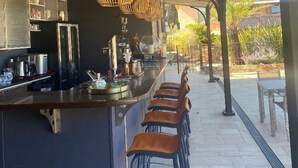 A covered outdoor bar area with a long counter, multiple stools, and hanging wicker light fixtures. - Bastide de Ramatuelle (Ramatuelle)