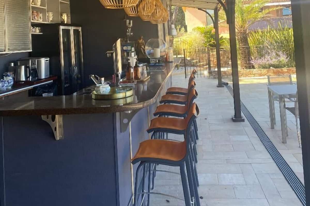 A covered outdoor bar area with a long counter, multiple stools, and hanging wicker light fixtures.