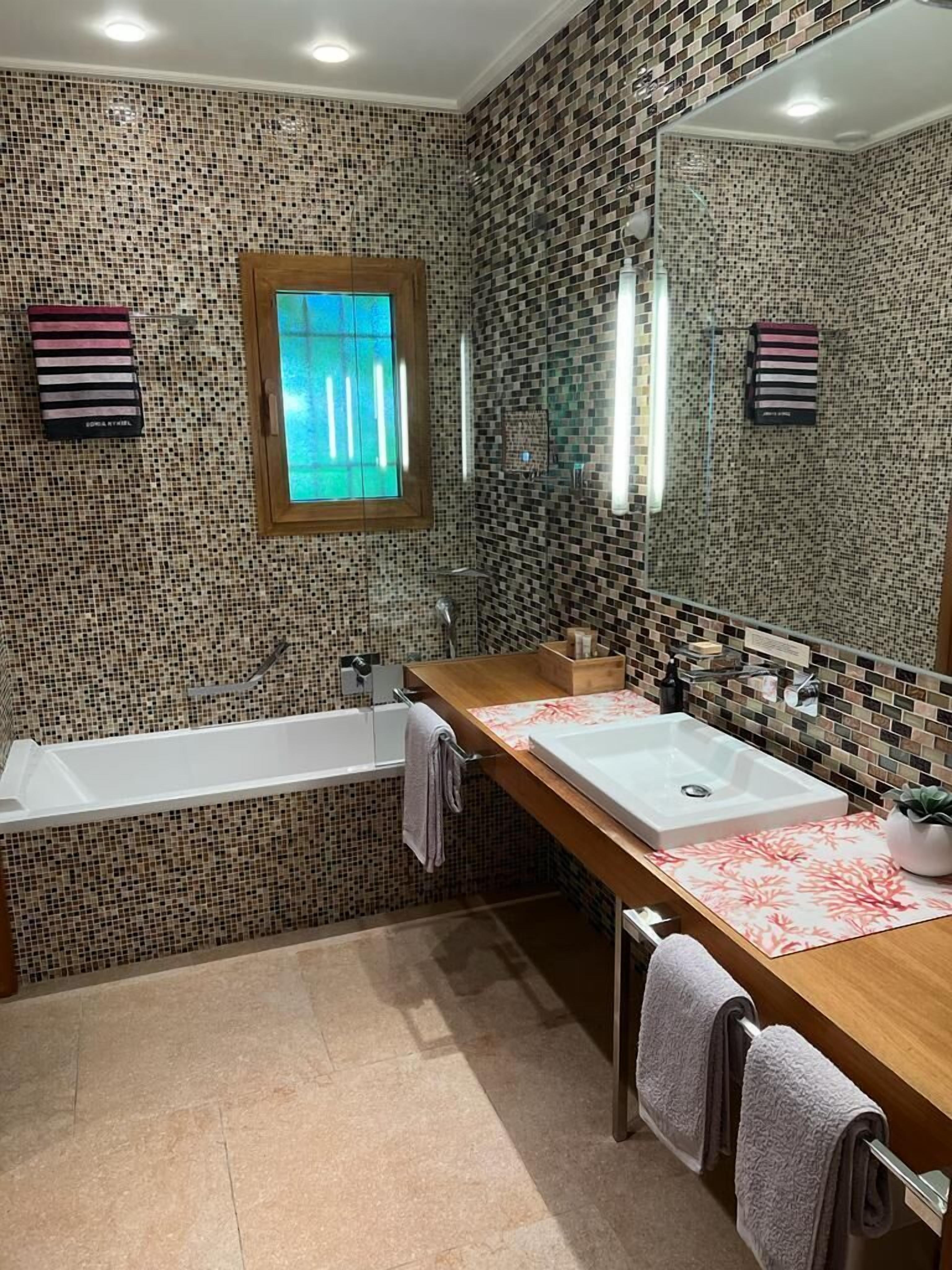 Ein Badezimmer mit einem großen Spiegel, zwei Waschbecken, einer Badewanne und einem Fenster.
